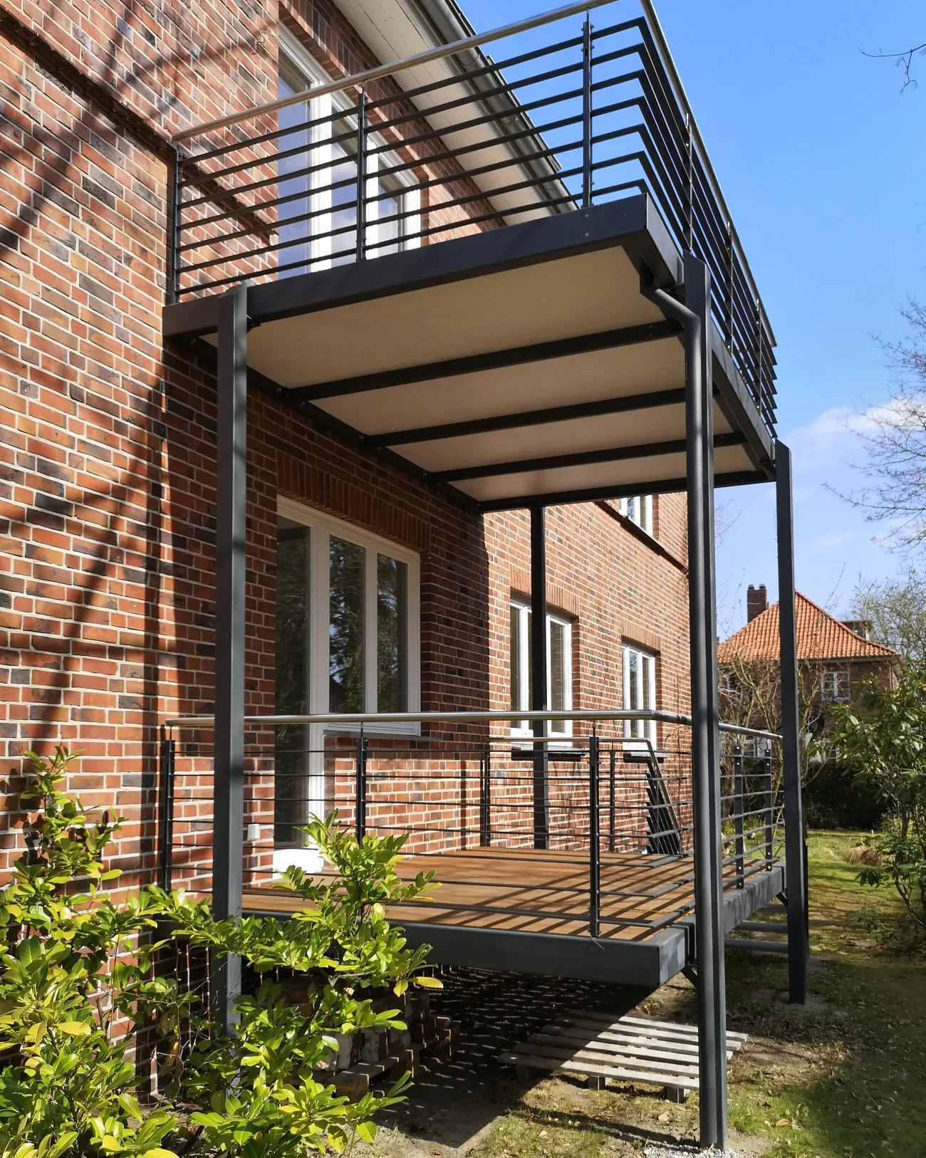 Zweigeschossiger Anbaubalkon in Anthrazit mit waagerechtem Stabgeländer, Edelstahlhandlauf und Holzbelag an einer Klinkervilla. Gebaut in Lüneburg.