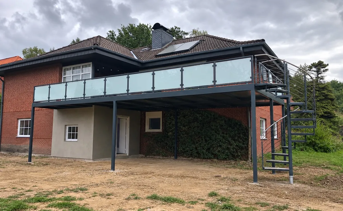 Balkon auf Stützen mit Glasgeländer und Wendeltreppe an einem Klinkerhaus mit Walmdach, davor der frisch planierte Garten. Gebaut in Vastorf.