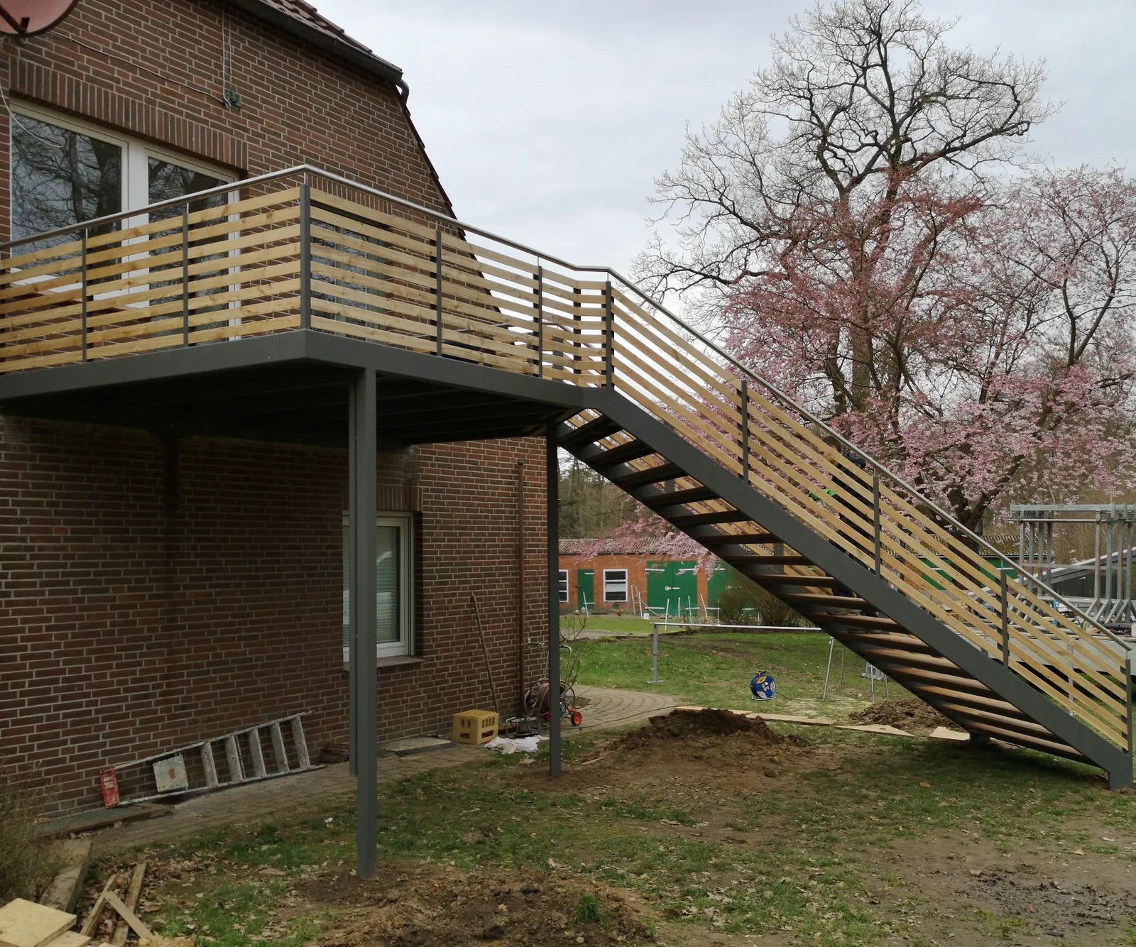 Balkon mit Geländer aus Holzlatten und langer Treppe in den Garten an einem Klinkerhaus, kurz nach der Montage. Gebaut in Dahlenburg.