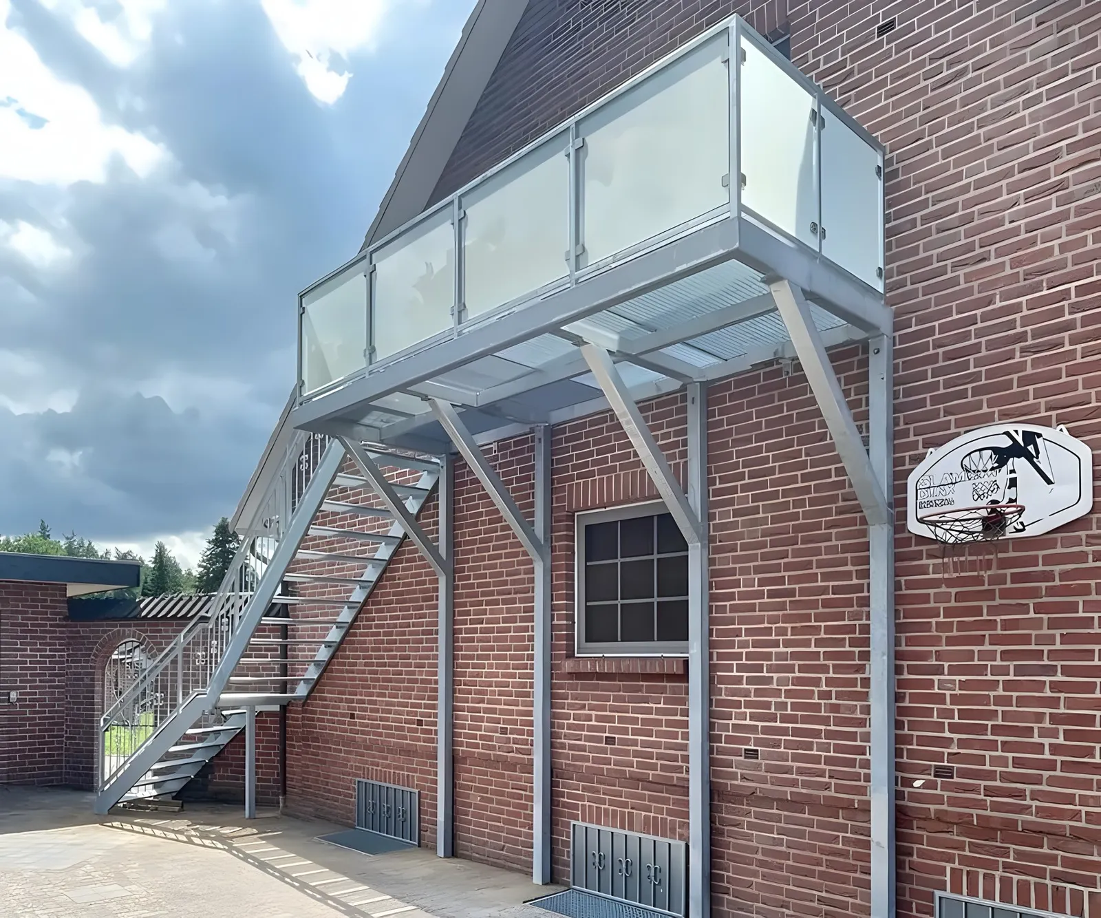 Feuerverzinkter Balkon mit Milchglasgeländer und Außentreppe an einer Klinkerfassade, mit Schrägstreben zur Wand. Gebaut in Bienenbüttel.