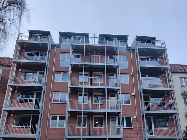 Neubau mit fünf Geschossen und vorgestellten Balkontürmen aus verzinktem Stahl mit Stabgeländer vor einer Klinkerfassade.