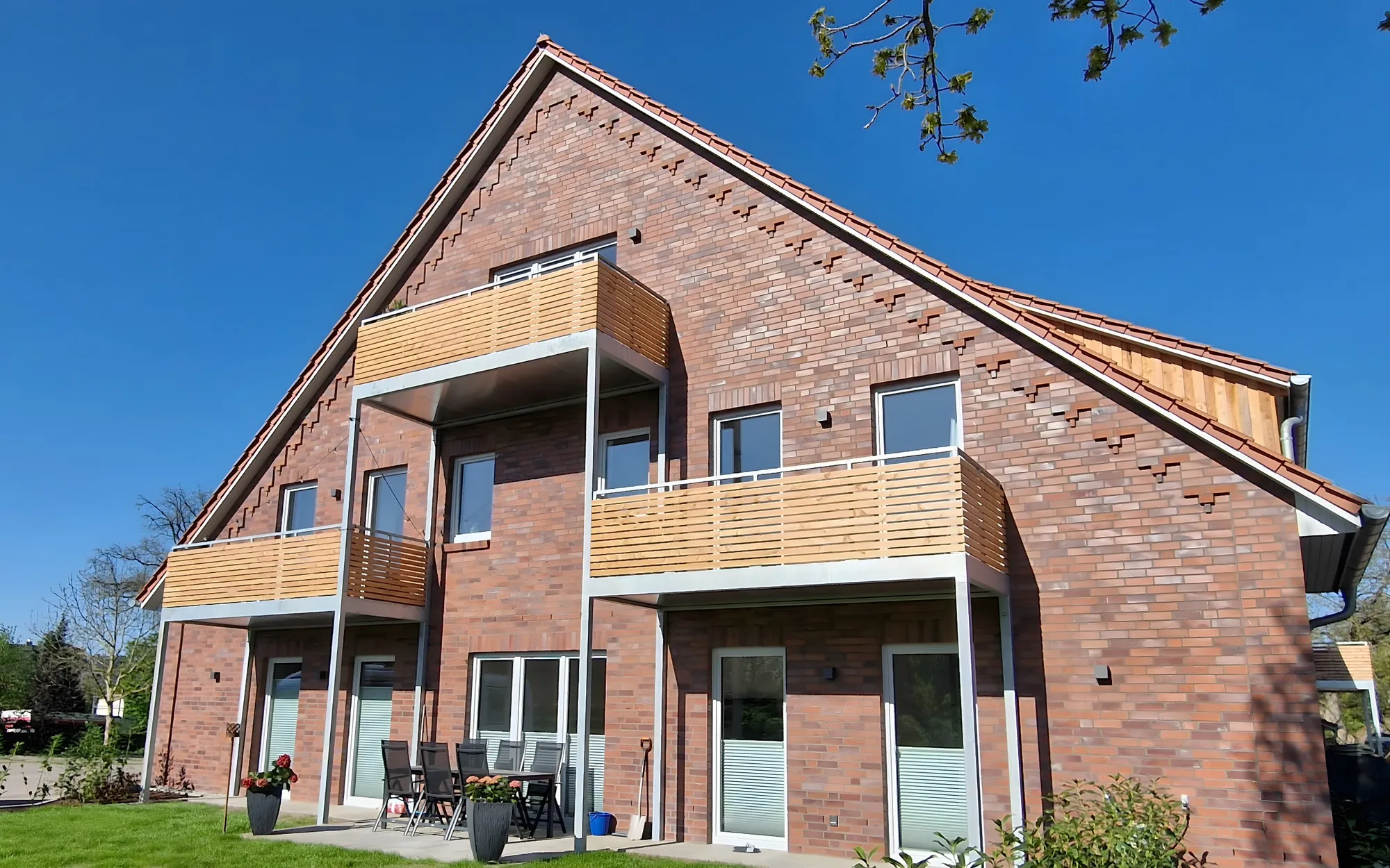 Zwei Balkone mit Holzverkleidung an einem Neubau aus rotem Klinker mit steilem Giebel, auf schlanken Stützen. Gebaut in Boltersen.