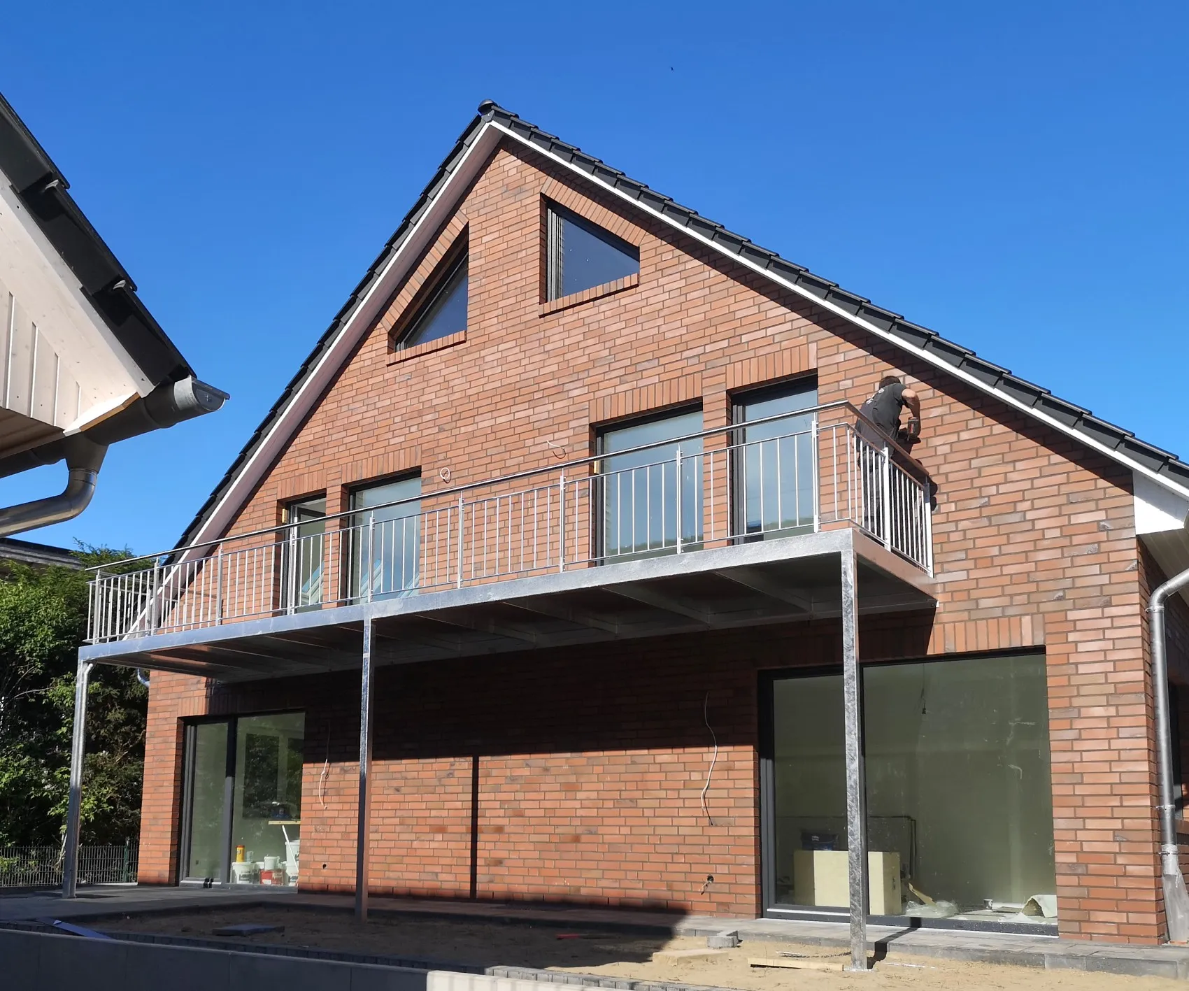 Langer Balkon mit verzinktem Stabgeländer an der Giebelseite eines neuen Klinkerhauses, getragen von schlanken Stützen. Gebaut in Seevetal.
