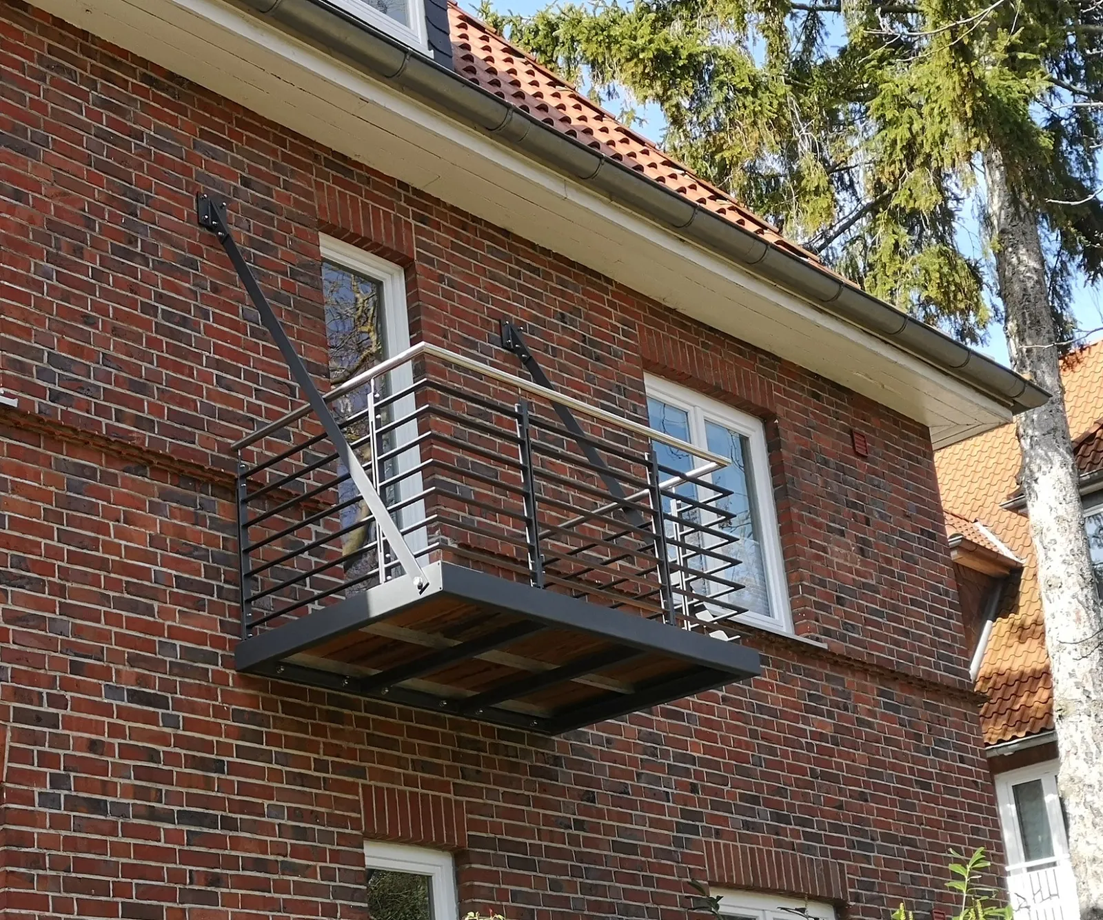 Kleiner Hängebalkon mit Zugstangen und waagerechtem Stabgeländer in Anthrazit an einer Klinkervilla. Gebaut in Lüneburg.