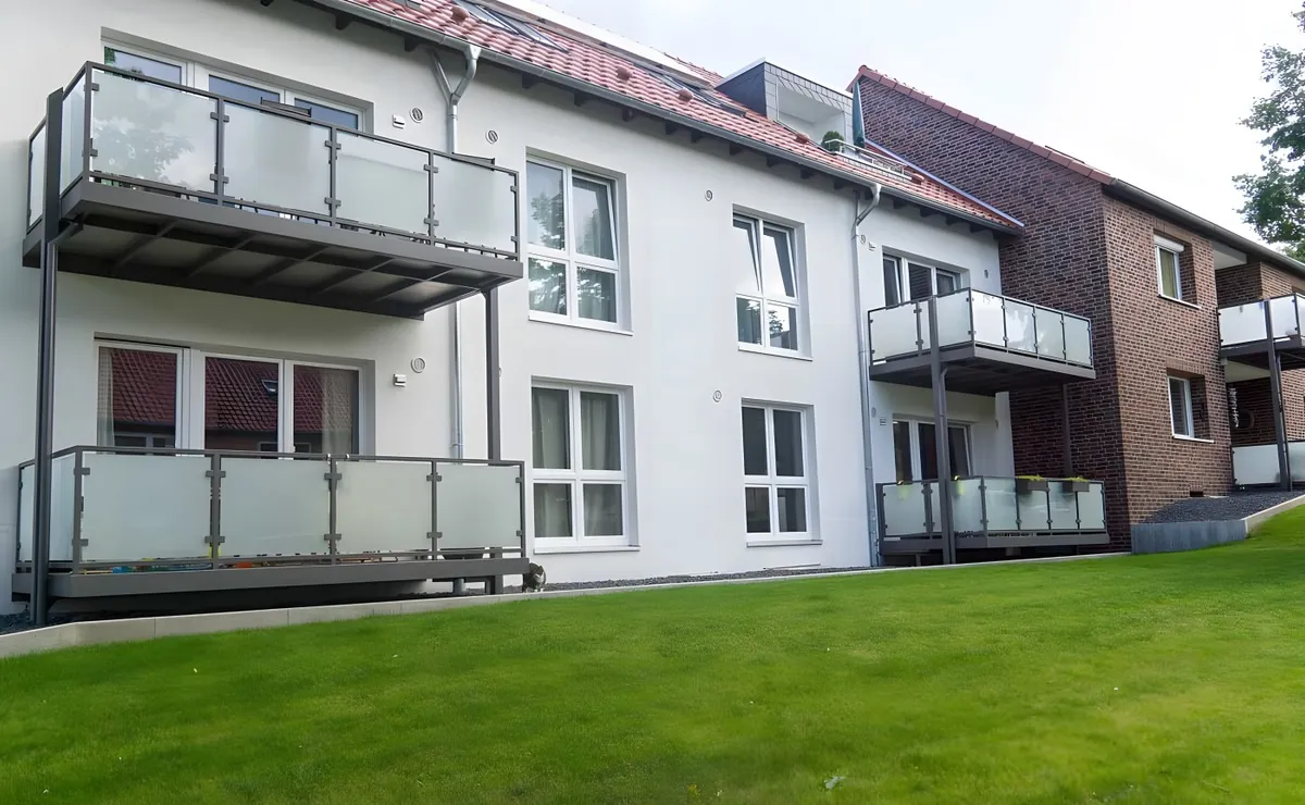 Balkone mit Milchglasgeländer an einem weißen Mehrfamilienhaus mit angrenzendem Klinkerbau. Gebaut in Lüneburg.