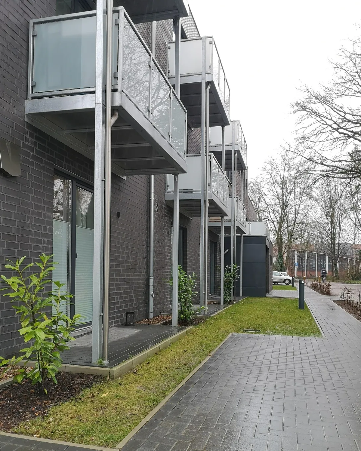 Übereinanderliegende Balkone mit Milchglasgeländer an einem Mehrfamilienhaus mit dunklem Klinker. Gebaut in Lüneburg.