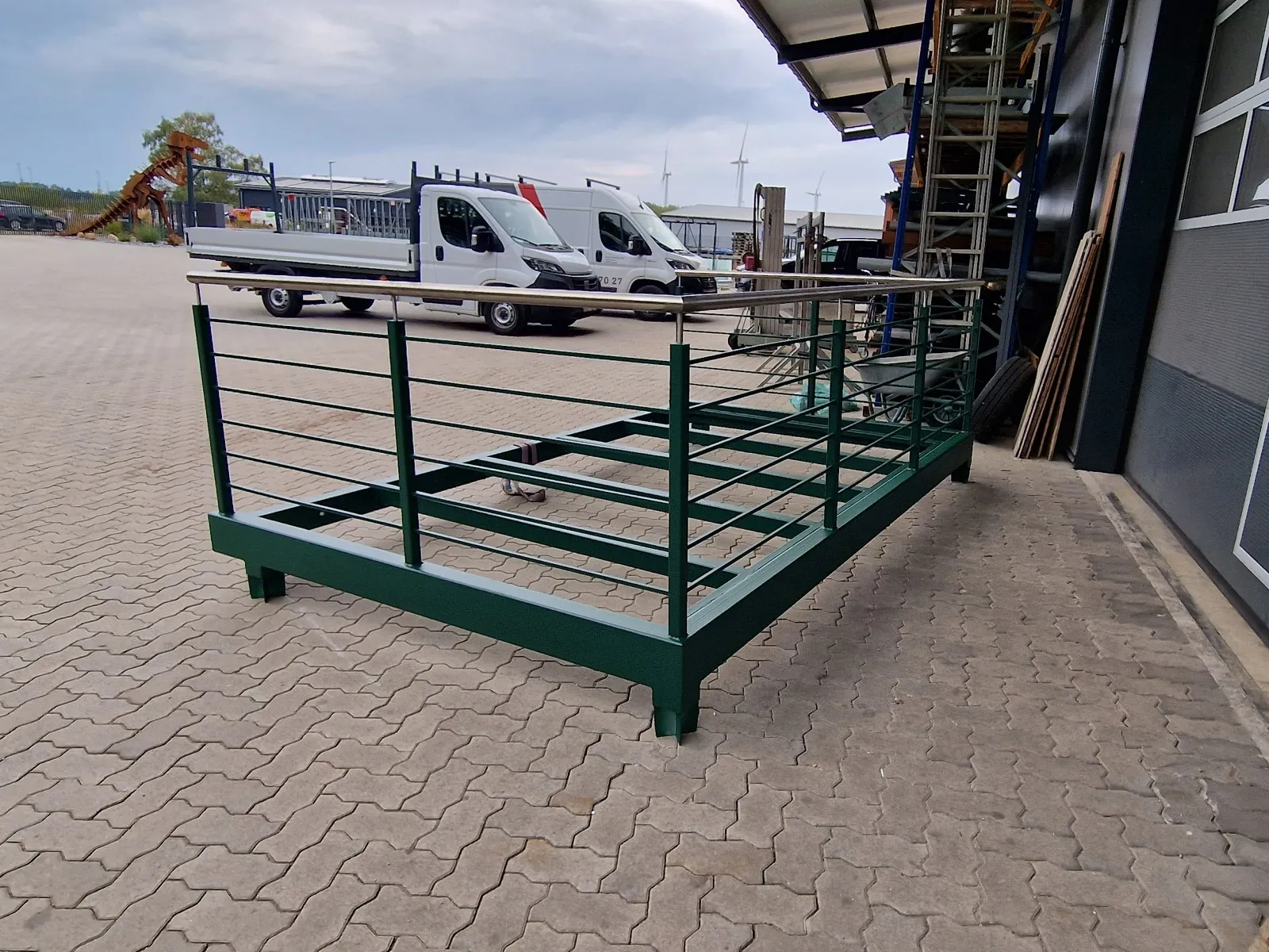 Fertig beschichteter grüner Balkon mit Relinggeländer und Edelstahl-Handlauf auf dem Hof vor der Werkhalle, dahinter Firmentransporter.