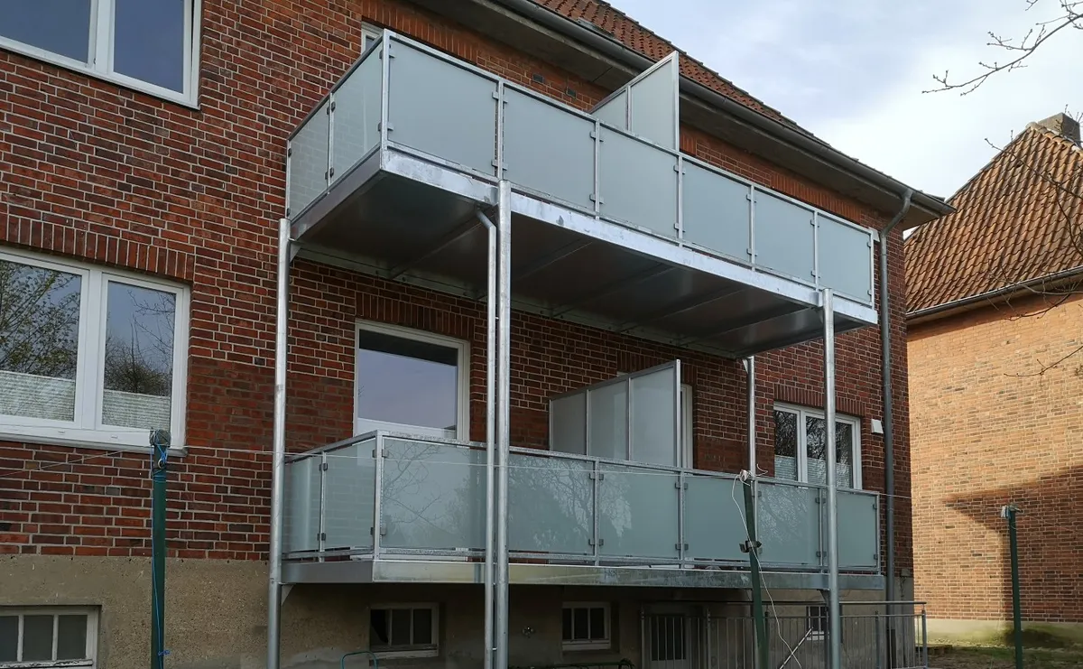 Zwei verzinkte Balkone übereinander mit satiniertem Glasgeländer und gläsernem Sichtschutz an einem Klinkerhaus. Gebaut in Lüneburg.