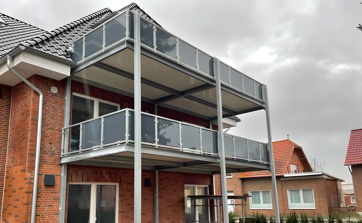 Zwei übereinanderliegende Balkone mit Glasgeländer auf durchgehenden Stützen an einem Klinkerhaus. Gebaut in Artlenburg.